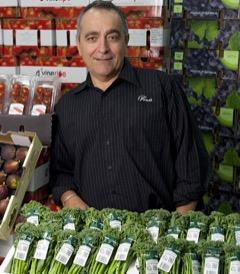 Michael Simonetta standing behind bunches of Broccolini, with produce boxes stacked behind him.